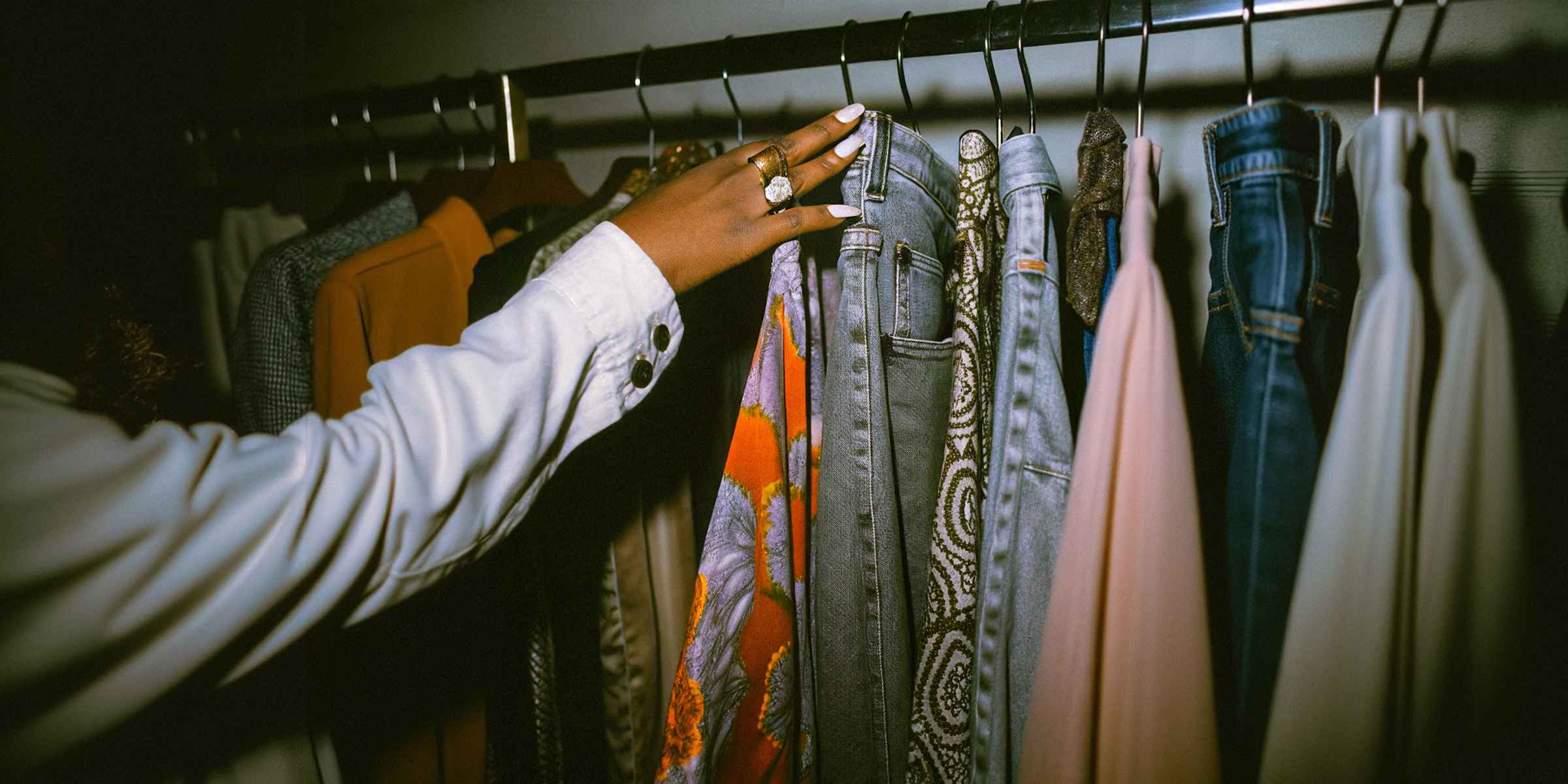 Beste-duftmaschinen-einzelhandel-hand-an-kleiderstange | zaluti b. V. Nahaufnahme einer hand, die unter sanfter beleuchtung durch verschiedene stoffe und farben an einer kleiderstange gleitet; duftmaschinen sorgen für eine einladende atmosphäre.