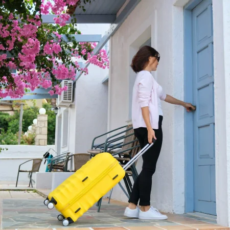 Vrouwelijke toerist met gele koffer gaat huis binnen
