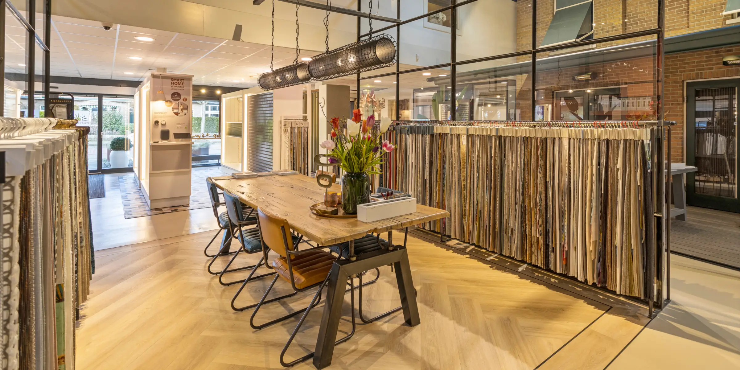 Scent-marketing-showroom-consultation-table-with-curtain-samples | zaluti b. V. Spacious showroom with a long wooden consultation table, a bouquet of tulips and a rack of curtain samples – an example of scent marketing in a showroom.