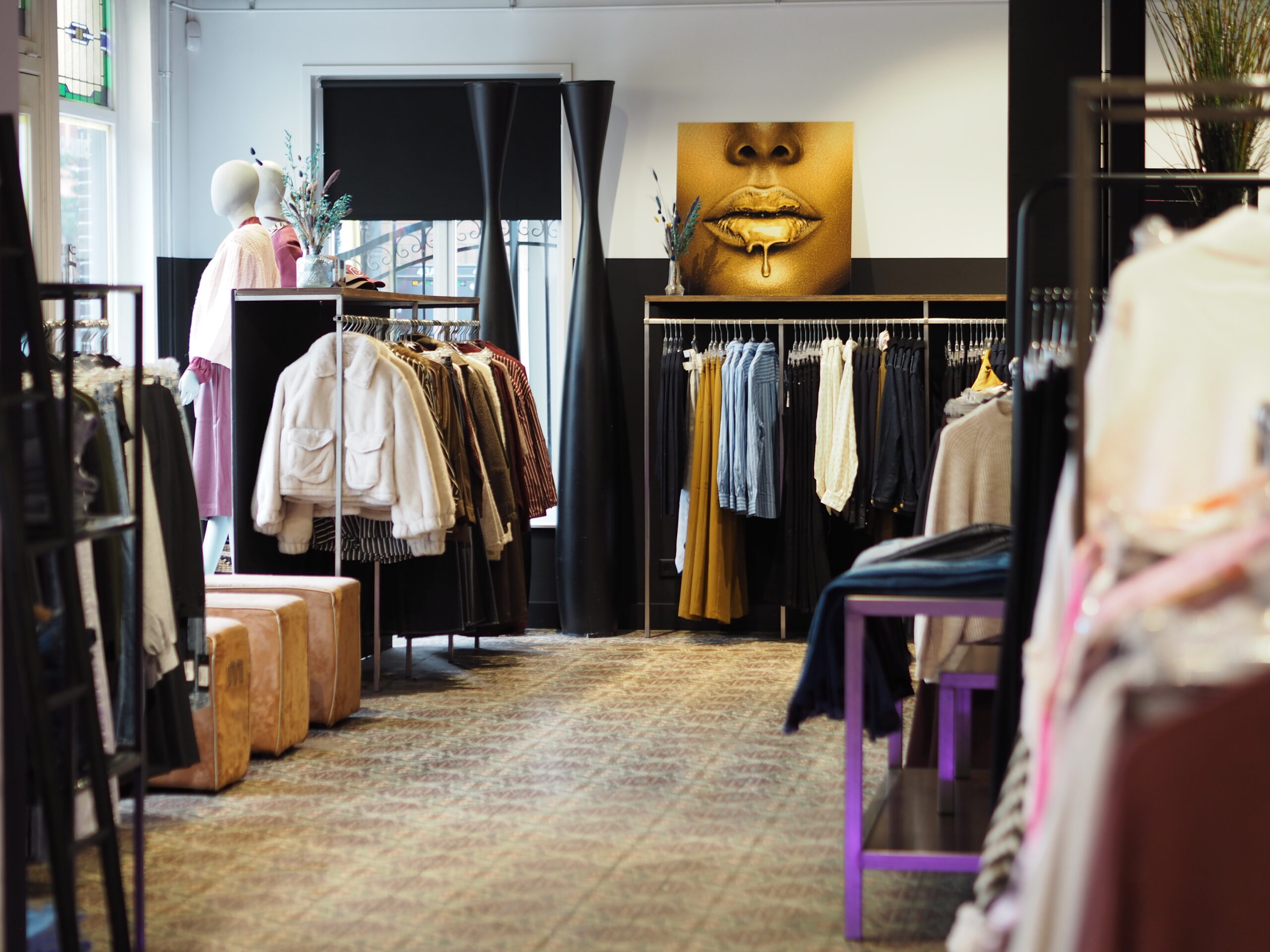 Cosy boutique with mannequins by the window, a golden artwork on the wall and racks of clothing; scent marketing creates a pleasant shopping experience.