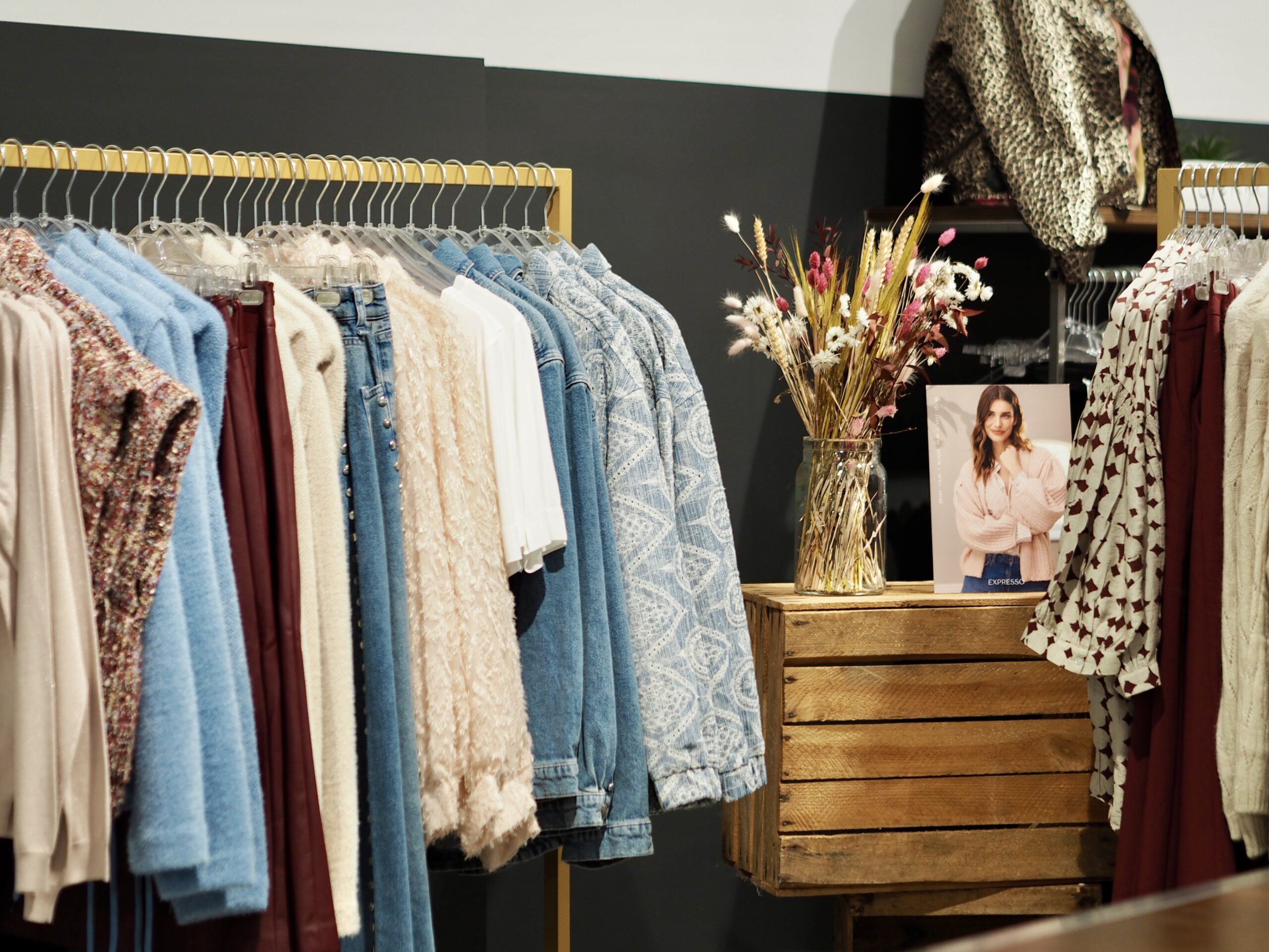 Spacious fashion store with orderly clothing racks, a table with folded sweaters and a calm colour scheme; scent marketing can enhance the shopping experience.
