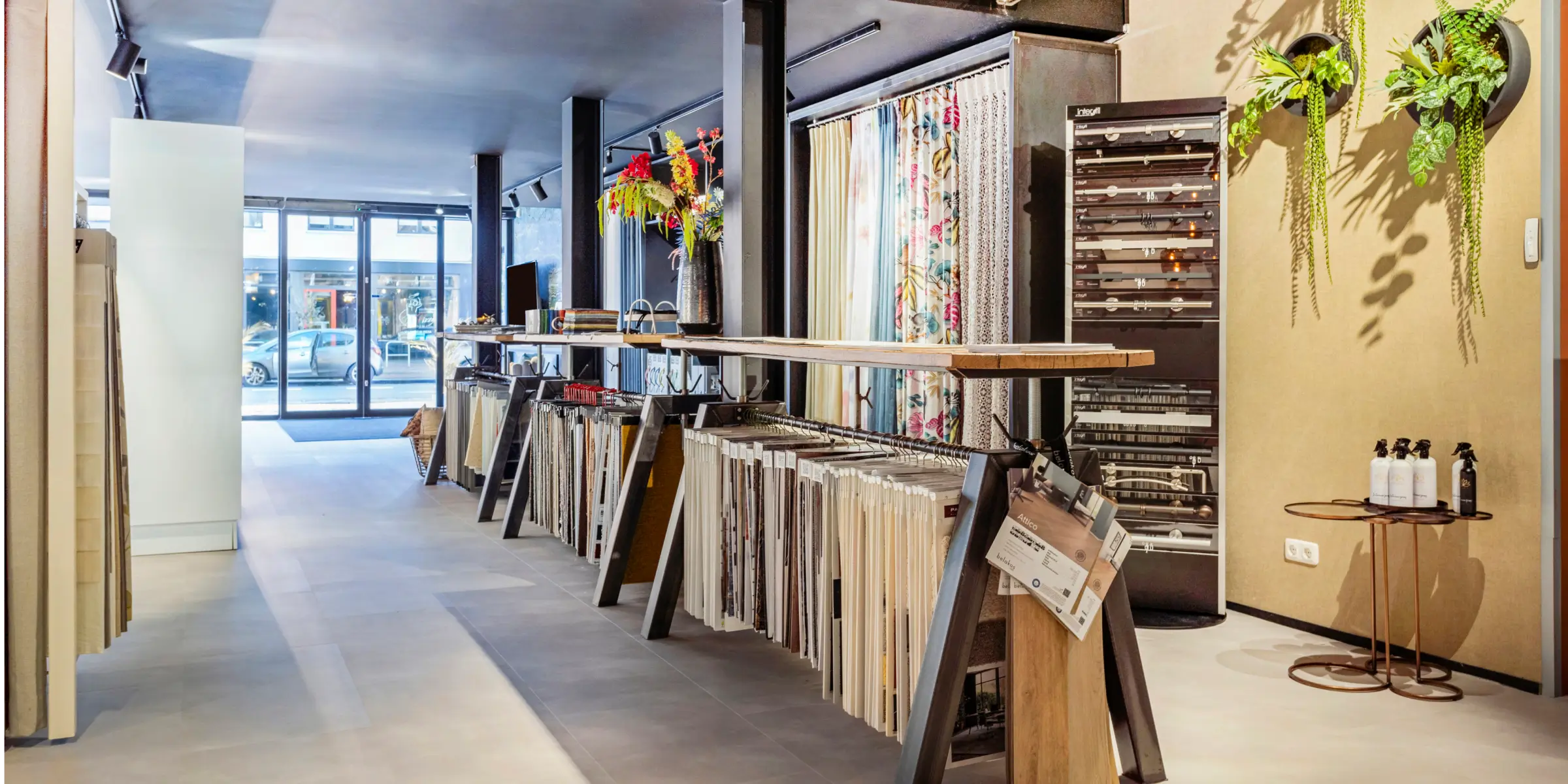 Scent-marketing-showroom-hallway-with-floor-samples-and-plants | zaluti b. V. Sleek showroom corridor with racks of floor samples, hanging plants and natural light where scent marketing subtly enhances the ambiance.