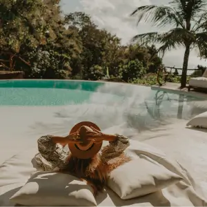 Woman is lying by a hotel swimming pool with palm trees