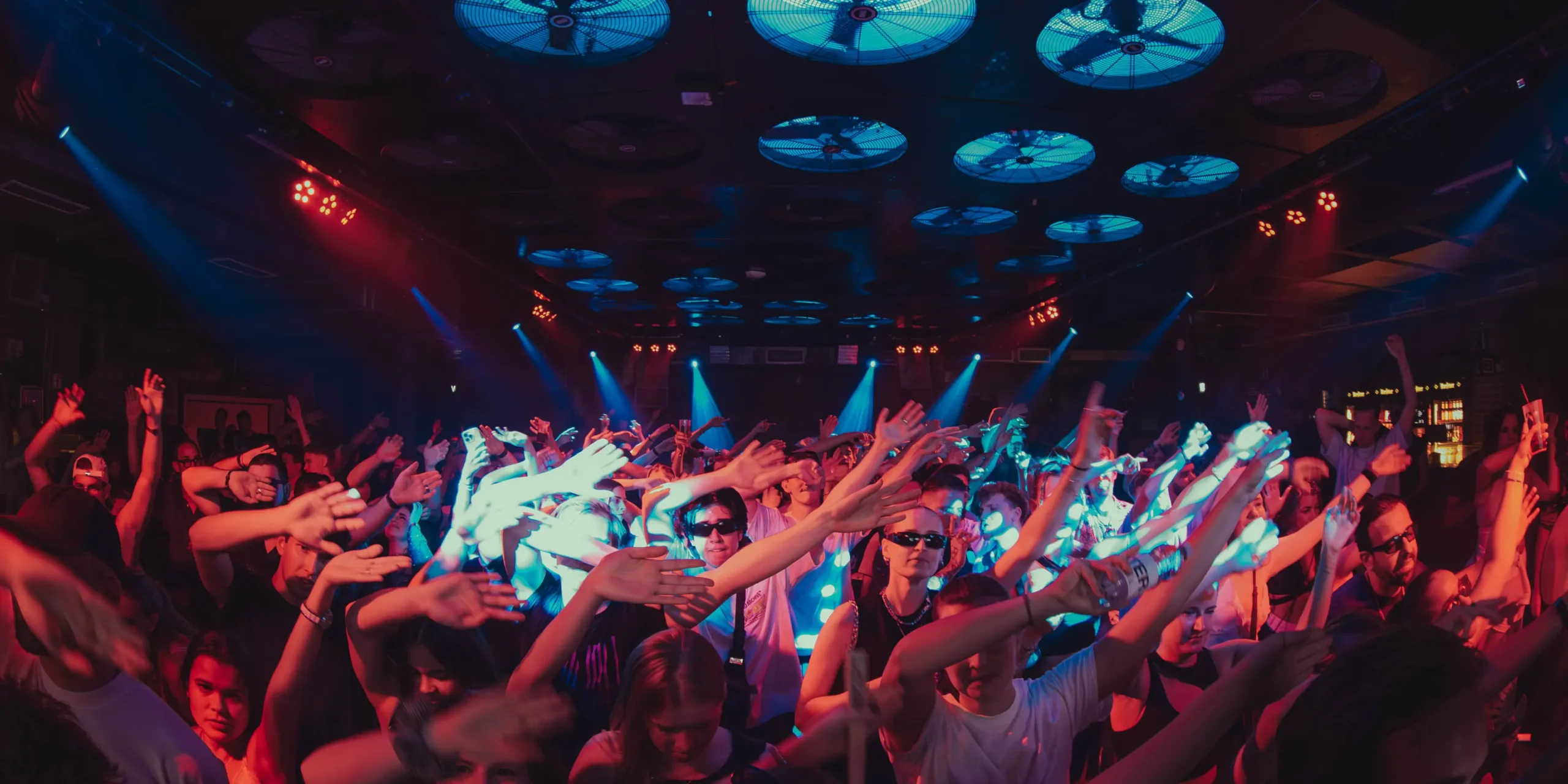 Odour-neutralization-dancing-crowd-with-ceiling-fans | zaluti b. V. Dancing crowd under large ceiling fans with hands in the air; effective odor neutralization helps keep the air fresh.