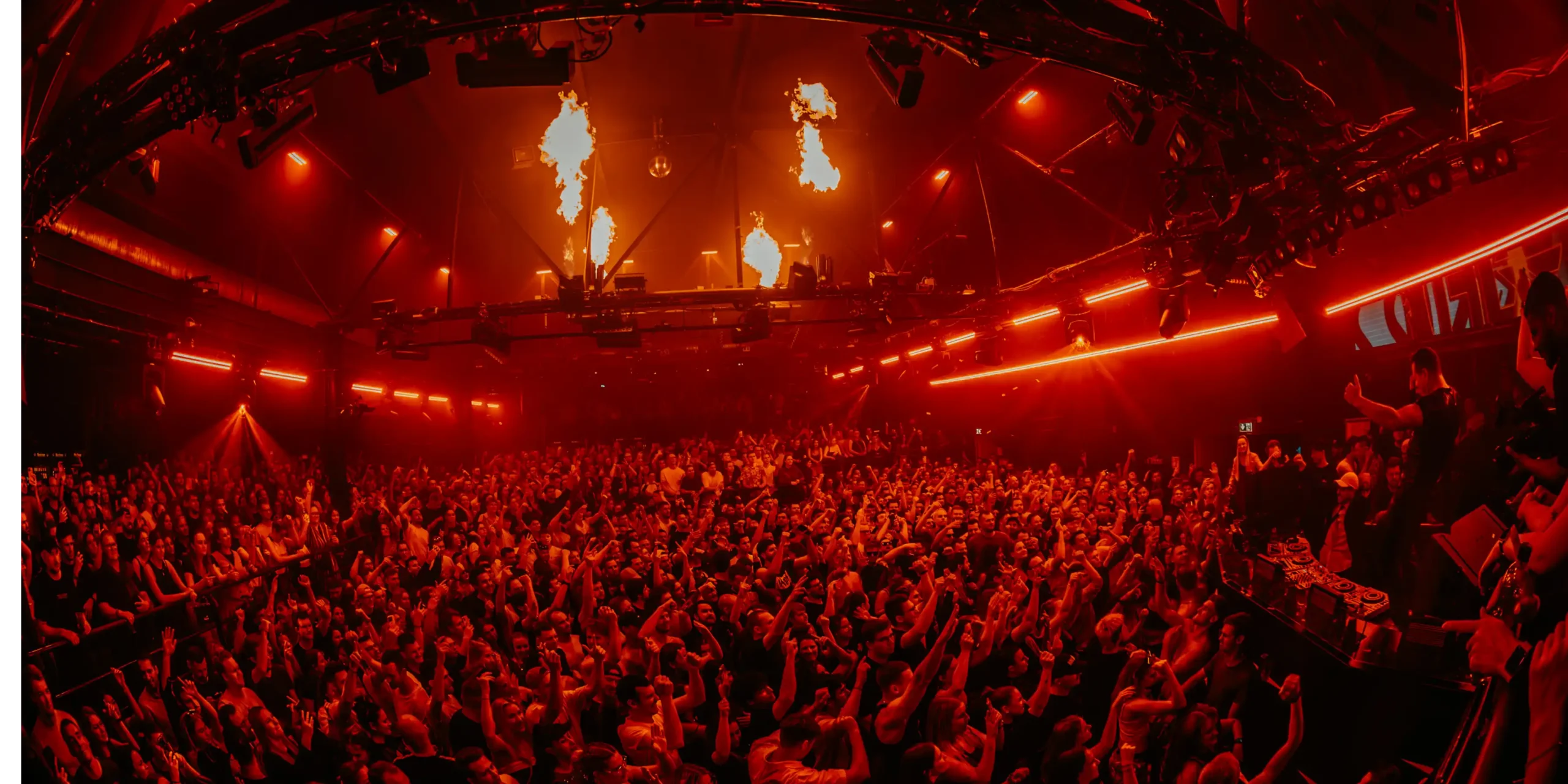 Club with red lighting and flames on the stage, surrounded by a cheering crowd; odor neutralization is important in hot and crowded venues.