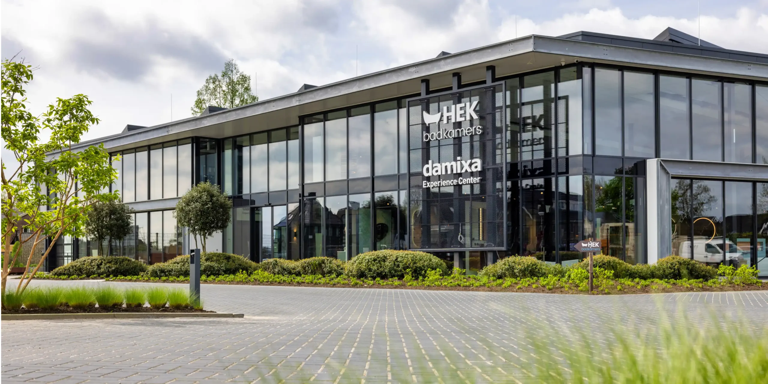 The modern glass façade of the hek bathrooms and damixa experience center with large windows, greenery and an inviting entrance where the scent experience welcomes visitors.